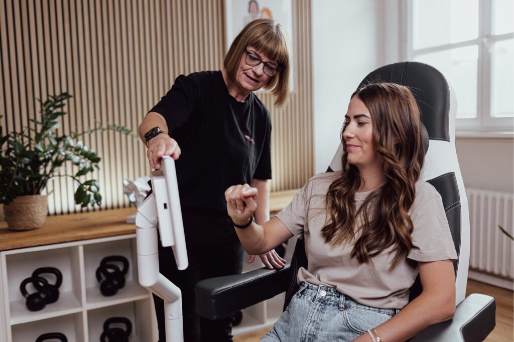 Ältere Frau erklärt Jüngerer Frau Funktionen eines Geräts zum Beckentraining gegen Inkontinenz.